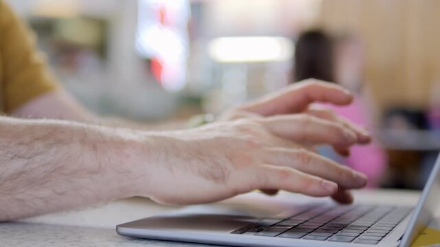 Hands type on laptop keyboard. Focus on fingers moving quickly. Background blurred with people nearby. Suggests work, communication, or online activity. Ideal for business, education, or tech themes