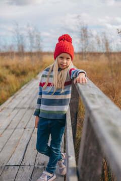 Cute girl in cozy clothing resting on a rural boardwalk in autumn