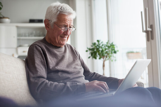 Portrait of senior man sitting on couch at home using laptop
