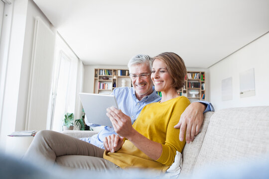 Smiling couple sitting on the couch at home using digital tablet