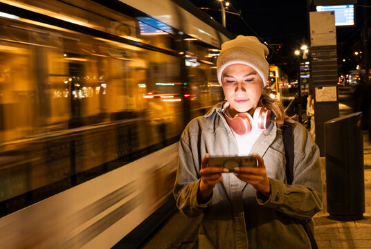 Woman in beanie using mobile phone at tram station at night