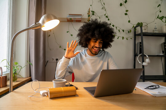 Happy freelancer waving on video call through laptop at home