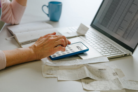 Woman calculating home budget and taxes using smartphone and laptop