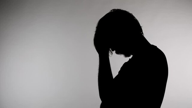Anonymous silhouette of a person holds head and shows signs of stress in a dimly lit room during evening hours