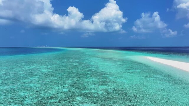 Aerial view of a pristine white sandbar surrounded by turquoise coral reefs and deep blue ocean waters under a cloudy sky in Kendhoo, Baa Atoll, Maldives.