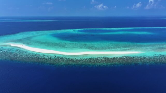 Aerial view of a pristine white sandbank surrounded by turquoise coral reefs and the deep blue Indian Ocean under a clear sky in Kendhoo, Baa Atoll, Maldives.