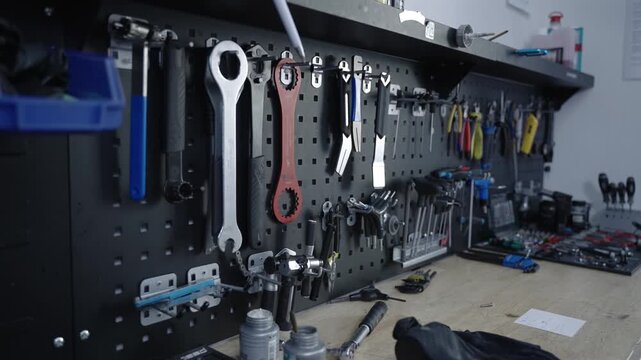 Professional bicycle tools organized on a black pegboard wall in a modern repair workshop. Specialized equipment, hex keys and wrenches on a clean mechanical workbench for bike maintenance service.