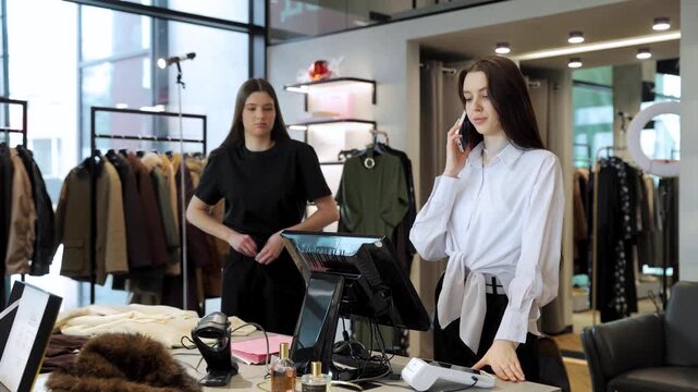 Woman working at retail store using smartphone, managing online orders or customer inquiries near register desk