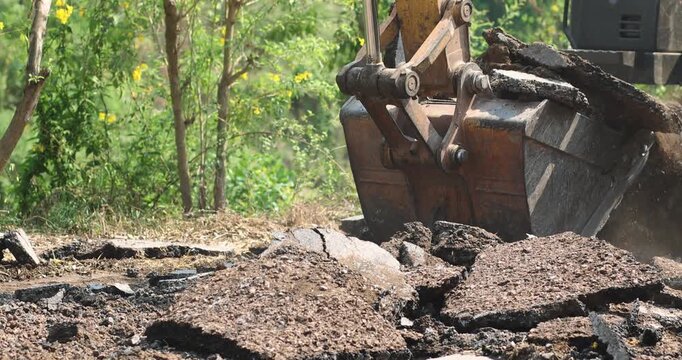 Excavator Digging Up Road Surface, Road construction and demolition, Excavator bucket digging, lifting broken asphalt and concrete debris, Excavator loading broken concrete at construction site