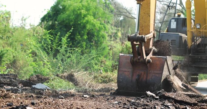Excavator Digging Up Road Surface, Road construction and demolition, Excavator bucket digging, lifting broken asphalt and concrete debris, Excavator loading broken concrete at construction site