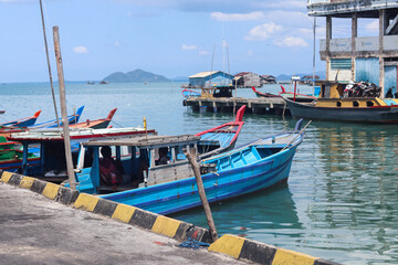 Obraz premium Traditional blue wooden fishing boats moored along a waterfront harbor with calm reflective water, working vessels, pier structures, and coastal maritime activity in a small fishing community 