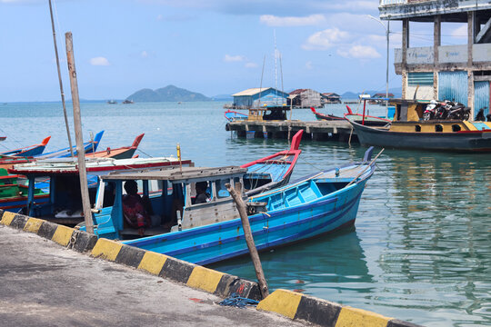 Traditional blue wooden fishing boats moored along a waterfront harbor with calm reflective water, working vessels, pier structures, and coastal maritime activity in a small fishing community 