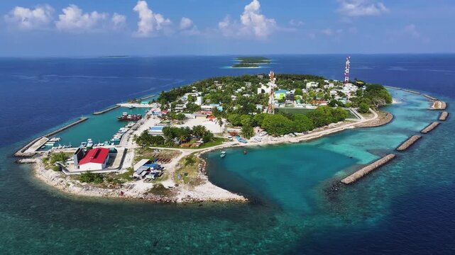 Aerial view of Kendhoo island featuring its harbor, coral reefs, and lush tropical vegetation under a clear blue sky in Kendhoo, Baa Atoll, Maldives.