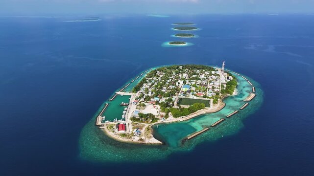 Aerial view of the tropical island of Kendhoo with its harbor, rooftops, and surrounding turquoise coral reefs in the deep blue ocean, Kendhoo, Baa Atoll, Maldives.