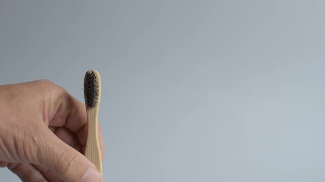 A hand removes a plastic toothbrush and replaces it with a bamboo toothbrush against a light gray studio background during a product video session to illustrate sustainable consumer choices, eco-frien