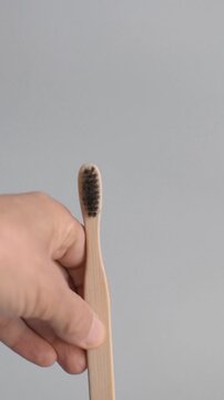 A hand removes a plastic toothbrush and replaces it with a bamboo toothbrush against a light gray studio background during a product video session to illustrate sustainable consumer choices, eco-frien