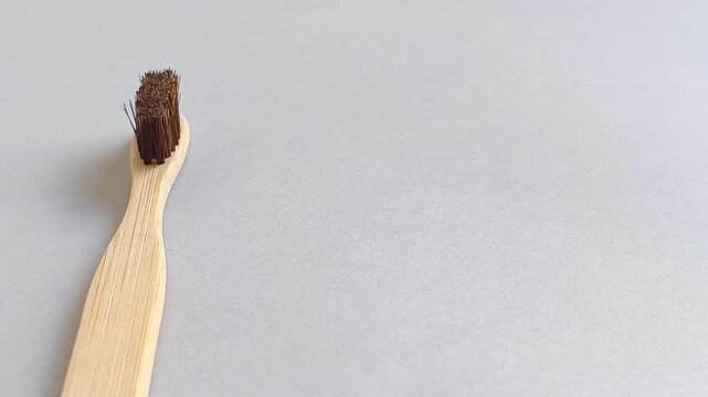 A bamboo toothbrush is filmed on a light gray studio background while the camera slowly pans from the handle to the bristles during a product video session to showcase sustainable oral care, natural m