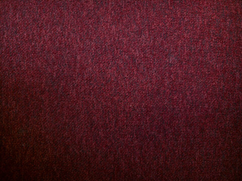 Dark red carpet texture background. Close-up of burgundy fabric, rug, or upholstery material with a woven pattern and subtle dark vignette edges.