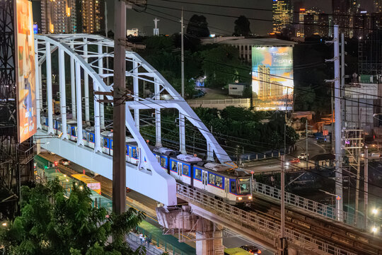 Pasay, Metro Manila Philippines - 2025 July 12: A commuter train of the Manila Metro Rail Transit System Line 3 (MRT-3) traveling on a truss bridge at night with city light backgrounds.