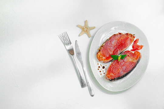 Raw salmon steaks on a ceramic plate garnished with mint, with cutlery on a white background