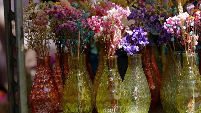 Delicate dried gypsophila flowers, also known as baby's-breath, in small colorful glass vases arranged on a shelf for sale in a market