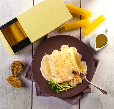 Meat cannelloni with b&eacute;chamel sauce on a brown plate. The packaging is next to the plate.
