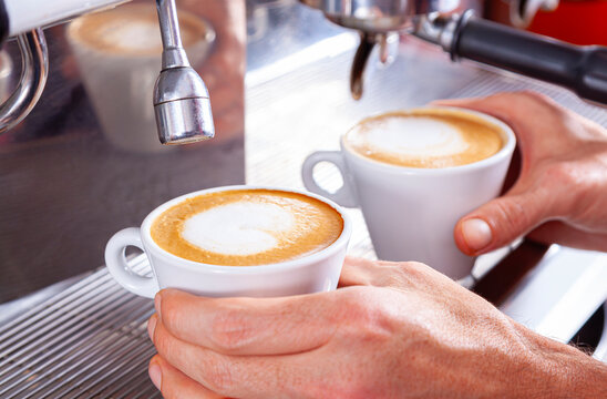 Two hands holding two cups of freshly brewed coffee.