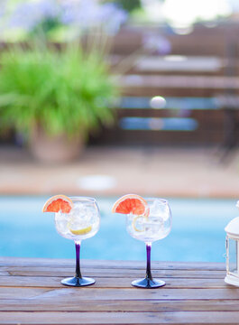 Two glasses with ice and a slice of grapefruit on a table by a pool