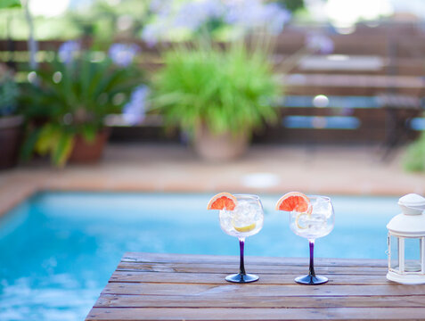 Two glasses with ice and a slice of grapefruit on a table by a pool