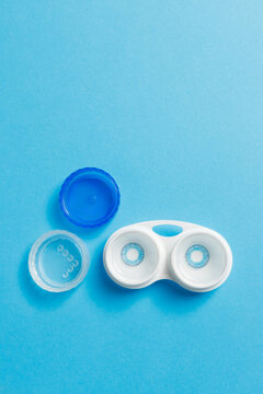 Vertical shot of open plastic contact lens case container with blue transparent caps on bright background, closeup top view portrait orientation concept of optometry ophthalmology eyesight care