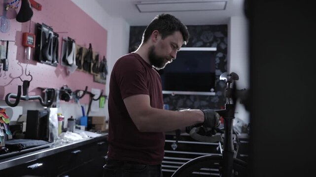Male technician performs precise overhaul of expensive black carbon road bike. Bicycle maintenance process, mechanical engineering skills, premium cycling equipment service in custom repair shop.