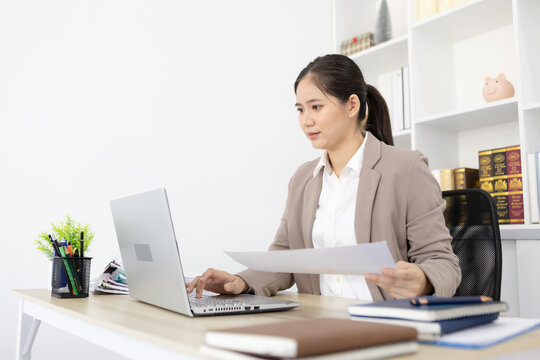 Woman types on laptop beside colorful charts. She focuses, showing professional engagement. Office setting implies analysis or presentation. Image works for business, finance, or data reporting
