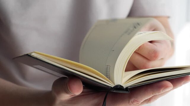 Paper pages in a notebook. A businessman holds a compact paper notebook with a bookmark in his hands.