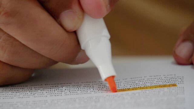 Man hand highlighting important text with brown marker in book at desk