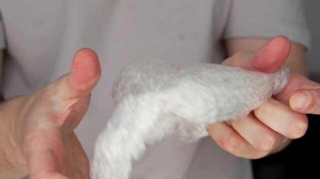 A guy holds bubble wrap.
He pops small bubbles on the transparent film with his fingers.