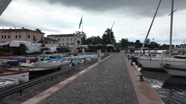 Bardolino, Italy - May 14, 2026 - Boats docked at a picturesque harbor with traditional buildings and cloudy skies