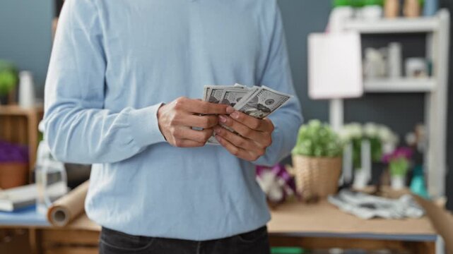 Man counting dollars with hands in flower studio surrounded by potted plants and wrapping paper; small business prosperity.
