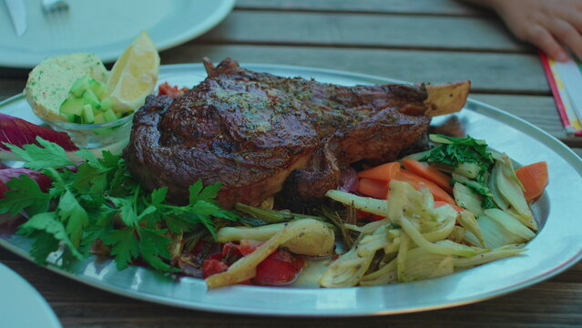 Large grilled steak platter with roasted vegetables served at outdoor restaurant capturing gourmet dining, hospitality and authentic upscale food presentation