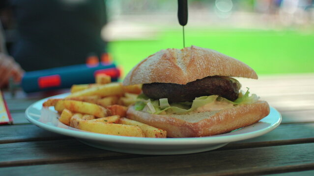 Hamburger with french fries served on outdoor cafe table capturing casual comfort food, fast dining culture and authentic restaurant lifestyle
