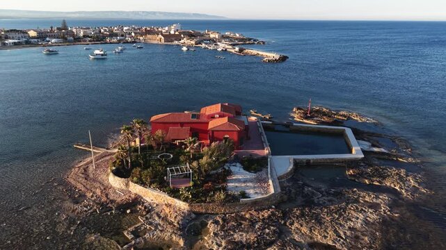 Aerial view of the red villa on Isolotto Brancati surrounded by the blue Mediterranean Sea near the coast of Marzamemi, Sicilia, Italy.