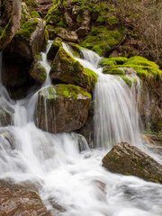 Beautiful waterfall cascading over mossy rocks in a lush spring forest © Akhmetova_m