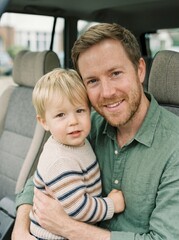Obraz premium Close up portrait of happy young father hugging his little blonde son inside car looking at camera