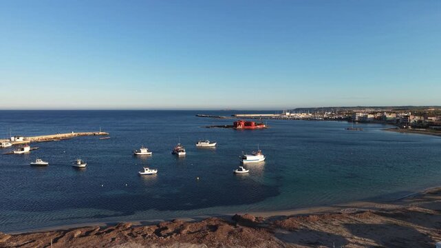 Aerial view of Isolotto Brancati and fishing boats anchored in the turquoise waters of the harbor in Marzamemi, Sicilia, Italy.