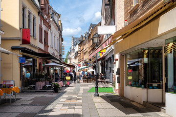 Fototapeta premium Pedestrian street with shops, cafes and outdoor dining in the historic center of Eltville on the Rhine beneath blue sky and clouds.