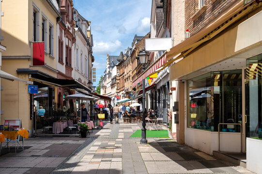Pedestrian street with shops, cafes and outdoor dining in the historic center of Eltville on the Rhine beneath blue sky and clouds.