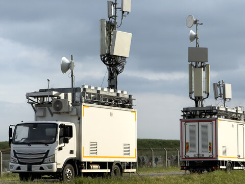 View of mobile telecommunications trucks with tall masts and satellite dishes parked in a grassy field under a cloudy sky in Besiktas, Istanbul, Turkiye.