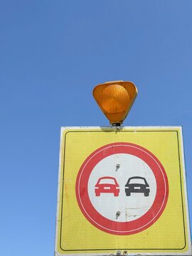 View of a no overtaking road sign with an orange flashing light on top against a clear blue sky in Sariyer, Istanbul, Turkiye.