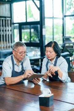 Senior asian couple restaurant owner reviewing income expense data using tablet discussing financial planning teamwork management collaboration family small business cooperation cafe lifestyle concept