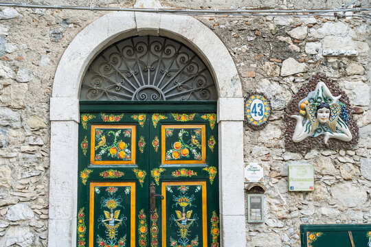 View of a traditional hand-painted green wooden door with Sicilian motifs and a ceramic Trinacria on a stone wall in Taormina, Sicily, Italy.