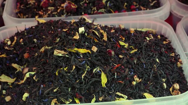 An assortment of loose leaf tea with flower petals and candied fruit on display at a market stall. Various types of tea for sale.